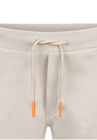 Beige joggings met een soepele textuur, voorzien van een trekkoord met oranje uiteinden en een ribbelband aan de taille.