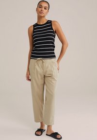 Black and white striped tank top with ribbed texture; beige relaxed-fit trousers with drawstring. Black slide sandals with knot detail.