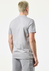 Tricou din bumbac gri, cu mâneci scurte și decolteu rotund, detalii vizibile de cusut și o croială regulară. Purtați-l cu pantaloni gri asortați.