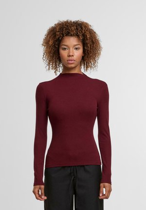 Top ajustado de manga larga burdeos con cuello alto, textura suave y costuras mínimas, combinado con pantalones negros sueltos.