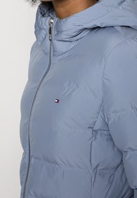 Chaqueta acolchada azul claro con cierre de cremallera, cuello alto y parche con logotipo. Confeccionada con material liso y brillante con costuras horizontales.