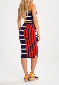 Bodycon šaty s námořnickými pruhy a výraznými červenými svislými liniemi, vyrobené z elastického materiálu. V kombinaci se žlutými espadrilami.