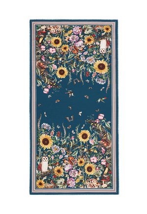 Kukkakuvioinen kangas, jossa auringonkukkia, pöllöjä, oravia, lintuja, perhosia ja sieniä sinisellä pohjalla, reunustettu raidallisella reunuksella.