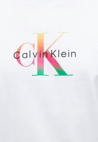 Λευκό ύφασμα με το λογότυπο Calvin Klein και μεγάλα γράμματα "cK" με διαβάθμιση πίσω από μικρότερο μαύρο κείμενο "Calvin Klein" στο κέντρο της επιφάνειας.