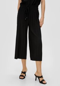 Zwarte geplooide culottes met een elastische tailleband en koord. Draagt deze met zwarte hakken. Glad stof met een vloeiende uitstraling.