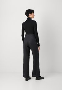 Juoda ilgo rankovė turtleneck marškiniai derinami su laisvai krentančiomis juodomis kelnėmis. Lygus paviršius, tiesaus kirpimo dizainas ir minimalistiškas stilius.