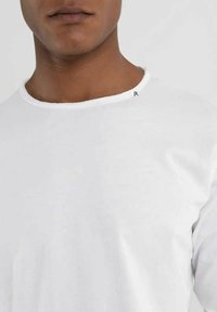 T-shirt bianco in cotone con scollo rotondo e un piccolo accento nero sul colletto. Il tessuto appare liscio e leggero.