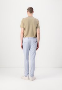 Tricou bej cu mânecă scurtă asortat cu pantaloni de culoare albastru deschis, având două buzunare pe spate cu cusături vizibile, completat de adidași albi.
