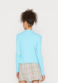 Camisola de mangas longas com nervuras em azul claro, com gola e barra ondulada. Combinada com uma saia mini xadrez em tons pastéis.