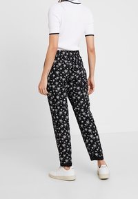 Pantalons noirs avec motif de palmiers blancs, taille élastique et jambes fuselées. Associés à un haut côtelé blanc et des baskets blanches.