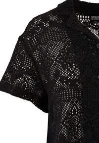 Schwarzes Häkeloberteil mit kurzen Ärmeln, Knopfverschluss und einem komplizierten Muster mit geometrischen und floralen Designs.