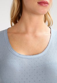 Ljusblå, ribbad stickad topp med rundad halsringning, vågiga kanter och ett strukturerat mönster av små prickar genom hela tyget.