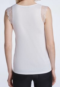 Top sin mangas blanco con detalles de encaje en los hombros, material suave y diseño ajustado, combinado con pantalones oscuros ajustados.
