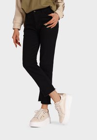 Jeans neri in denim a vita alta con orlo sfilacciato, abbinati a sneaker platform beige chiaro con dettagli testurizzati e suole bianche.