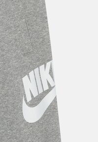 Šedé bavlněné tepláky s velkým bílým logem Nike a designem swoosh na levé straně. Tkanina má texturovaný povrch.