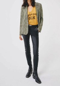 Grön mönstrad kavaj, gul grafisk t-shirt med "ROCK", svarta åtsittande byxor och svarta ankelskor med silverdetaljer.