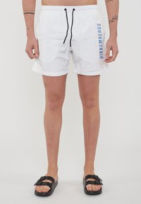 Witte zwembroek met zwarte trekkoord, met de tekst "BIKKENBERGS" in verloop van blauw en beige. Lichtgewicht, gladde stof, lengte tot de knie.