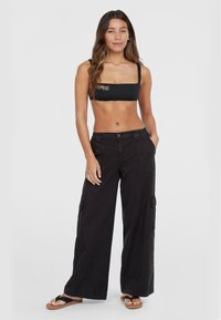 Zwarte crop top met decoratieve borduursels, gecombineerd met wijde zwarte cargobroeken met zijzakken en een ontspannen pasvorm.