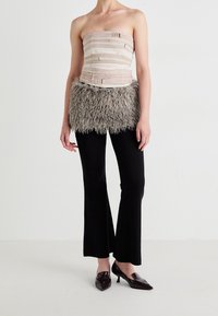 Trägerloses Oberteil mit hellrosa und weißen Streifen, gesichert mit Schnallen, kombiniert mit einem flauschigen grauen Federrock; schwarze, ausgestellte Hosen und glänzende Schuhe.