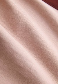 Tissu doux rose clair avec une texture fine tricotée, présenté en gros plan avec des plis doux et des ombres.