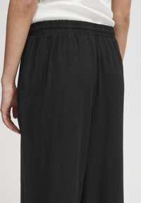 Melni brīvas formas bikses ar elastīgu jostu, kurām ir gluda, viegla tekstūra un plaša kāju dizains. Nav ievērojamu rakstu.