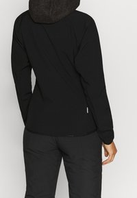 Schwarze Jacke mit langen Ärmeln und einer strukturierten, dunklen Kapuze. Verfügt über eine schlanke Passform, weiches Material und ein dezentes Logo nahe dem Saum.