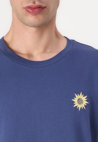 Navy blue cotton t-shirt featuring a yellow embroidered sun design on the left chest area. Crew neckline with ribbed texture.