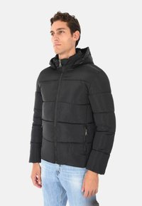 Giubbotto imbottito nero con cappuccio. Presenta segmenti trapuntati, chiusura frontale con zip e tasche laterali. Tessuto liscio e leggero.