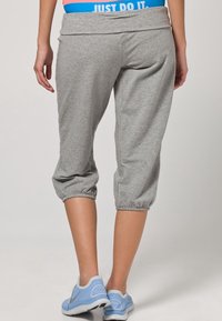 Pantaloni sportivi grigi a vita alta con polsini arricciati e una cintura ampia, che presenta un logo blu e bianco "JUST DO IT", abbinati a scarpe sportive blu.
