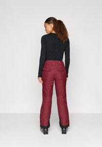 Bordeaux sneeuwbroek met een hoge taille, twee achterzakken en een elastische tailleband, ontworpen voor warmte en mobiliteit in koude omstandigheden.