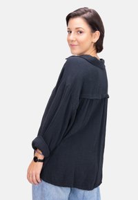 Bequeme, dunkelblaue Button-Up-Bluse aus strukturiertem Stoff mit hochgerollten Ärmeln und einem Rückeneinsatz. Kombiniert mit hellblauen Jeans.