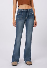 Flared blue jeans with a faded wash, featuring front pockets, a button closure, and frayed hems. Made from denim fabric.