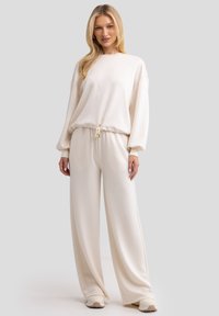 Conjunto de loungewear color crema que incluye un sudadera de corte suelto con cintura ajustable y pantalones de pierna ancha. Tejido suave y liso con puños bajos.