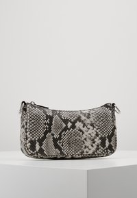 Czarna i biała torebka ze skóry wężowej o gładkiej fakturze, zaokrąglonym kształcie, zamknięciu na zamek błyskawiczny i srebrnych elementach ozdobnych.