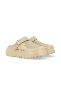 Zuecos beige sin cordones con una parte superior de malla texturizada, suela de goma y correa ajustable. Presentan orificios de ventilación a los lados para mayor transpirabilidad.