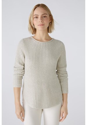 Hellgrauer gestrickter Pullover mit einem strukturierten Muster, langen Ärmeln und einem runden Halsausschnitt. Leicht verlängertes Rückenteil. Kombiniert mit hellen Hosen.