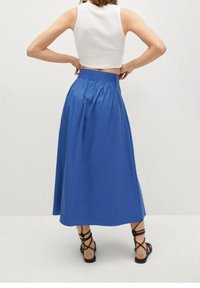 Gonna lunga blu con vita elastica arricciata, realizzata in un tessuto liscio. Indossata con una maglietta corta bianca e sandali neri con cinturini.