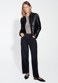 Giacca di pelle nera con tasche frontali, abbinata a una maglietta henley grigia chiara e jeans larghi neri. Ballerine nere a punta completano il look.