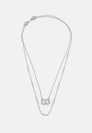 Srebrna ogrlica sa slojevima koja se sastoji od dva lanca, od kojih jedan ima geometrijski privjesak ukrašen malim prozirnim kristalima i kopčom na jastogu.