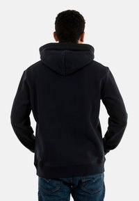 Sudadera negra con una gran capucha ajustable. Textura suave, puños y dobladillo acanalados. Presenta un diseño minimalista sin logotipos visibles.