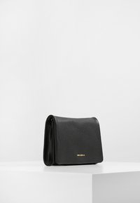 Czarna skórzana torebka o fakturze strukturalnej, prostokątnym kształcie i złotym logo z przodu, z klapką składana na górze.