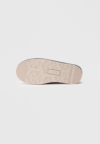 Suola della scarpa con un design testurizzato che presenta motivi a fiocco di neve. Il colore è beige chiaro con scanalature per una migliore aderenza. Il logo del marchio è visibile.