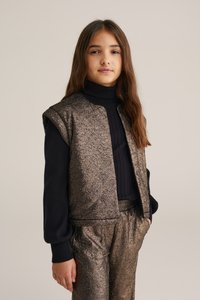 Bronsmönstrad ärmlös jacka över en marinblå ribbad polotröja, i sällskap med matchande byxor som har elastisk midja och sidofickor.