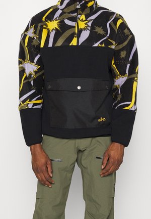 Polarowa bluza z wysokim kołnierzem; wyróżnia się żywą żółtą, fioletową i czarną kolorystyką; kontrastowy czarny panel z przodu z zapięciem na zatrzask.