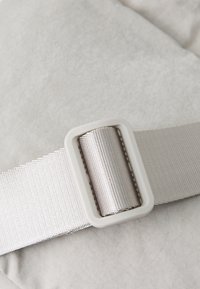 Gai pelēks audums ar maigu tekstūru, ar sudraba metāla sprādzi un plakanu, gludu siksnu.