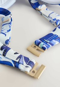 Bretele din țesătură cu model floral albastru și accesorii metalice aurii, având o textură netedă și un design reglabil pentru fixare.