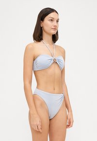 Svetlomodrý bikini set s bandeau topom a detailom uzla vpredu, doplnený striebornými prvkami a vysokým pásom spodných častí. Hladká textúra.
