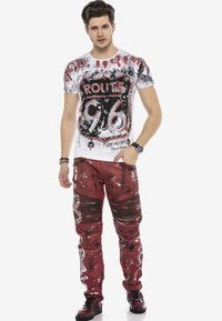 Weißes Grafik-T-Shirt mit rotem und schwarzem "Route 96"-Design, kombiniert mit roten, ausgewaschenen Hosen mit strukturierten Akzenten und Mustern.