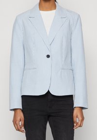 Pruhovaný světle modrý blazer s klopami, jedním knoflíkem vpředu, předními kapsami s patkami a texturovanou látkou. Dlouhé rukávy se stylovými liniemi.