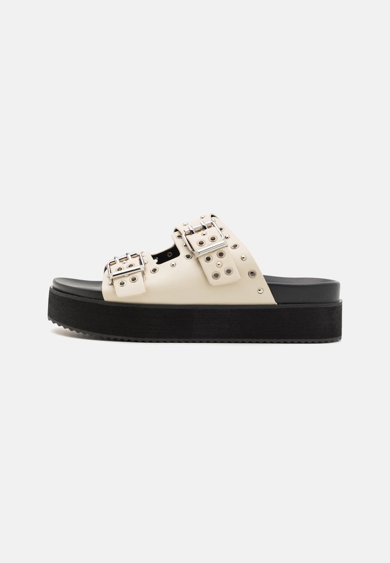 Sandales à plateforme en similicuir blanc cassé avec semelle noire. Equipées de deux boucles métalliques et d'accents de clous ronds pour plus de détails.